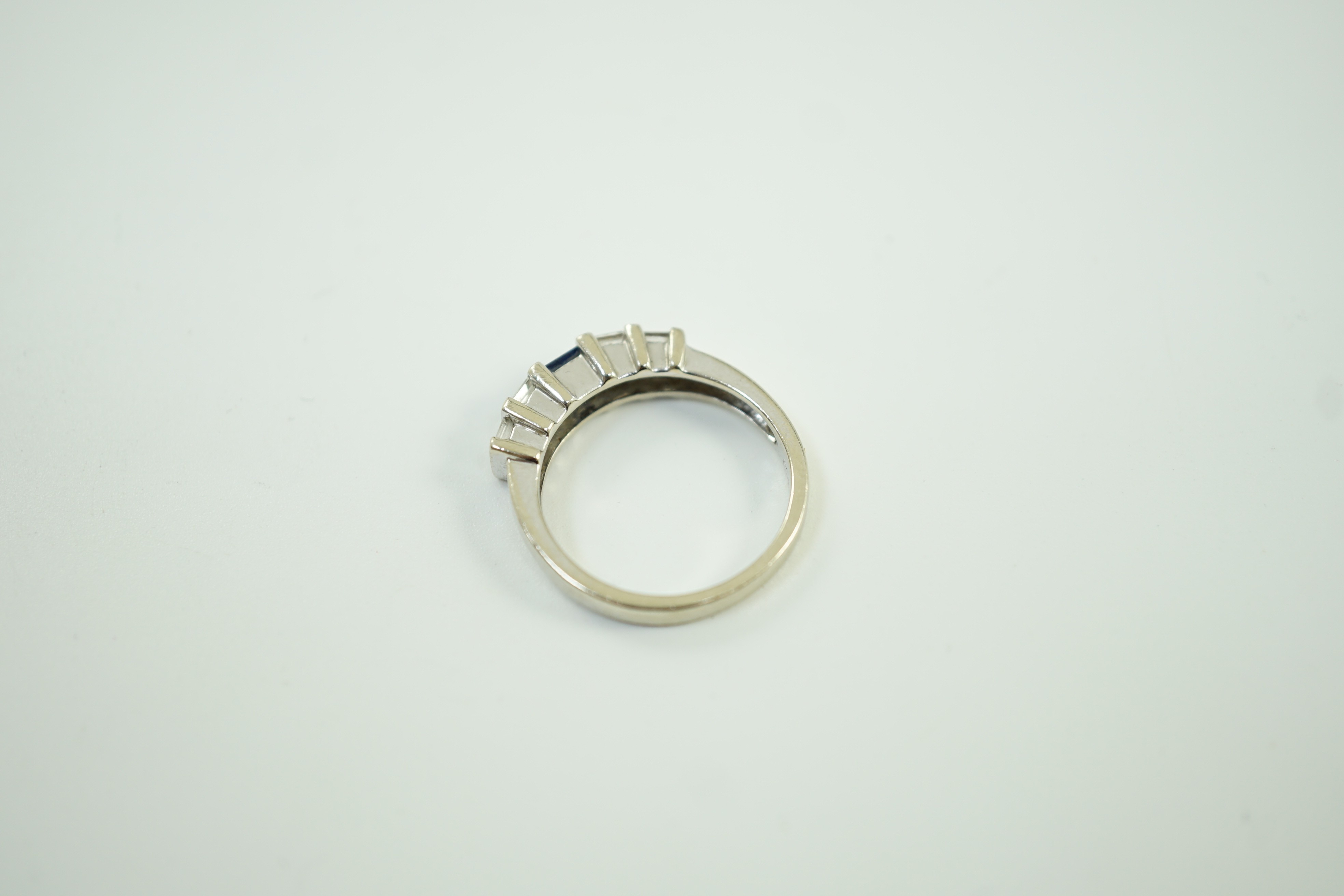 A modern 585 white metal, single stone sapphire and twelve stone baguette cut diamond cluster set half hoop ring, size N/O, gross weight 4 grams.